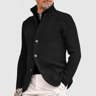 Beloza Cardigan in schwarz, mit einem eleganten Stehkragen und Knöpfen. Der Mann trägt den Cardigan zusammen mit einem schwarzen Hemd und einer beigen Hose, was einen modernen und stilvollen Look vermittelt.