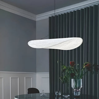 Eine moderne, energieeffiziente LED-Hängelampe in eleganter, geschwungener Form beleuchtet einen stilvollen Essbereich. Die Lampe hat eine weiche, warme Ausstrahlung und hängt über einem Tisch, auf dem ein Blumenstrauß in einer Glasvase steht. Der Raum ist von eleganten, grünen Vorhängen und einer minimalistischen Wandverkleidung umgeben, was die ruhige und raffinierte Atmosphäre des Raums unterstreicht.