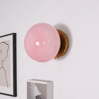 Eine zarte rosa Pendelleuchte mit einer glänzenden Kugelform und einer goldenen Wandhalterung. Diese elegante Leuchte verleiht Ihrem Raum eine warme, stilvolle Atmosphäre und passt perfekt in moderne Einrichtungskonzepte.