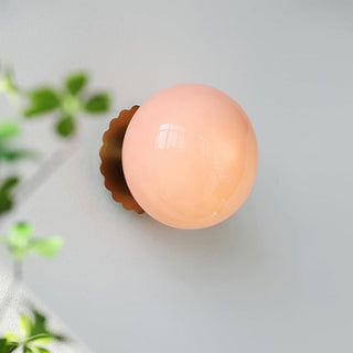 Eine stilvolle Pendelleuchte mit einer sanft rosa, glänzenden Kugel und einer goldenen Wandhalterung. Diese elegante Leuchte fügt sich perfekt in moderne Wohnräume ein und schafft eine gemütliche Atmosphäre.