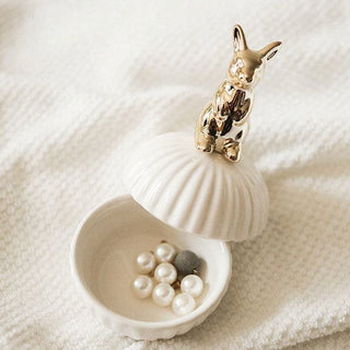Die Hilma Schmuckdose mit einem niedlichen Hasen-Design und einer Muschelform. Diese elegante und praktische Dose eignet sich perfekt zur Aufbewahrung von Schmuckstücken wie Perlen und kleinen Accessoires. Der goldene Hase auf dem Deckel verleiht der Dose einen charmanten und stilvollen Touch, ideal für das Badezimmer oder Schlafzimmer.