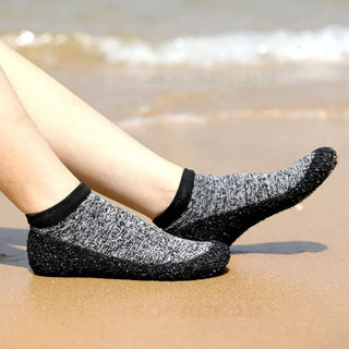 Xara Socken mit robuster Sohle am Strand getragen. Vielseitige, rutschfeste Socken in Schwarz-Grau, perfekt für Outdoor- und Freizeitaktivitäten. Angenehme Passform für maximalen Komfort und Stabilität auf verschiedenen Untergründen.